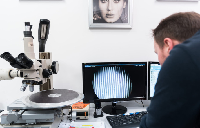 Dans l’un des studios, un employé DE MPO ausculte au microscope les vinyles retournés par les clients afin de vérifier s’ils sont effectivement défectueux et, le cas échéant, de rechercher l’origine du problème.