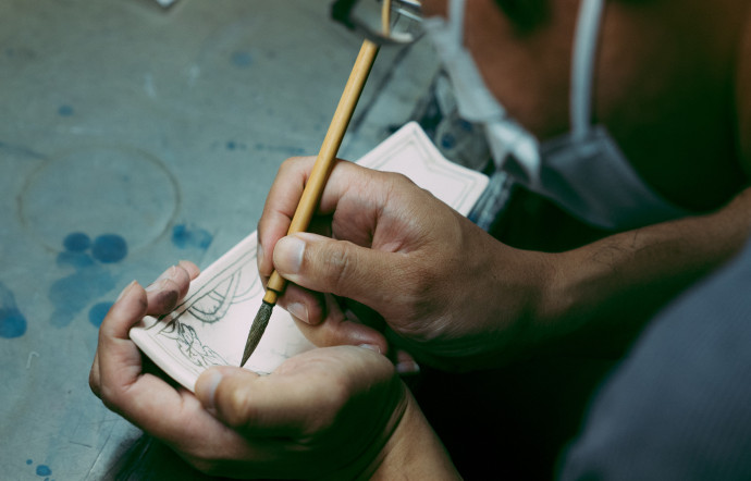 Un potier local en plein travail de peinture des motifs de MURAYAMA Macoto sur de la porcelaine.